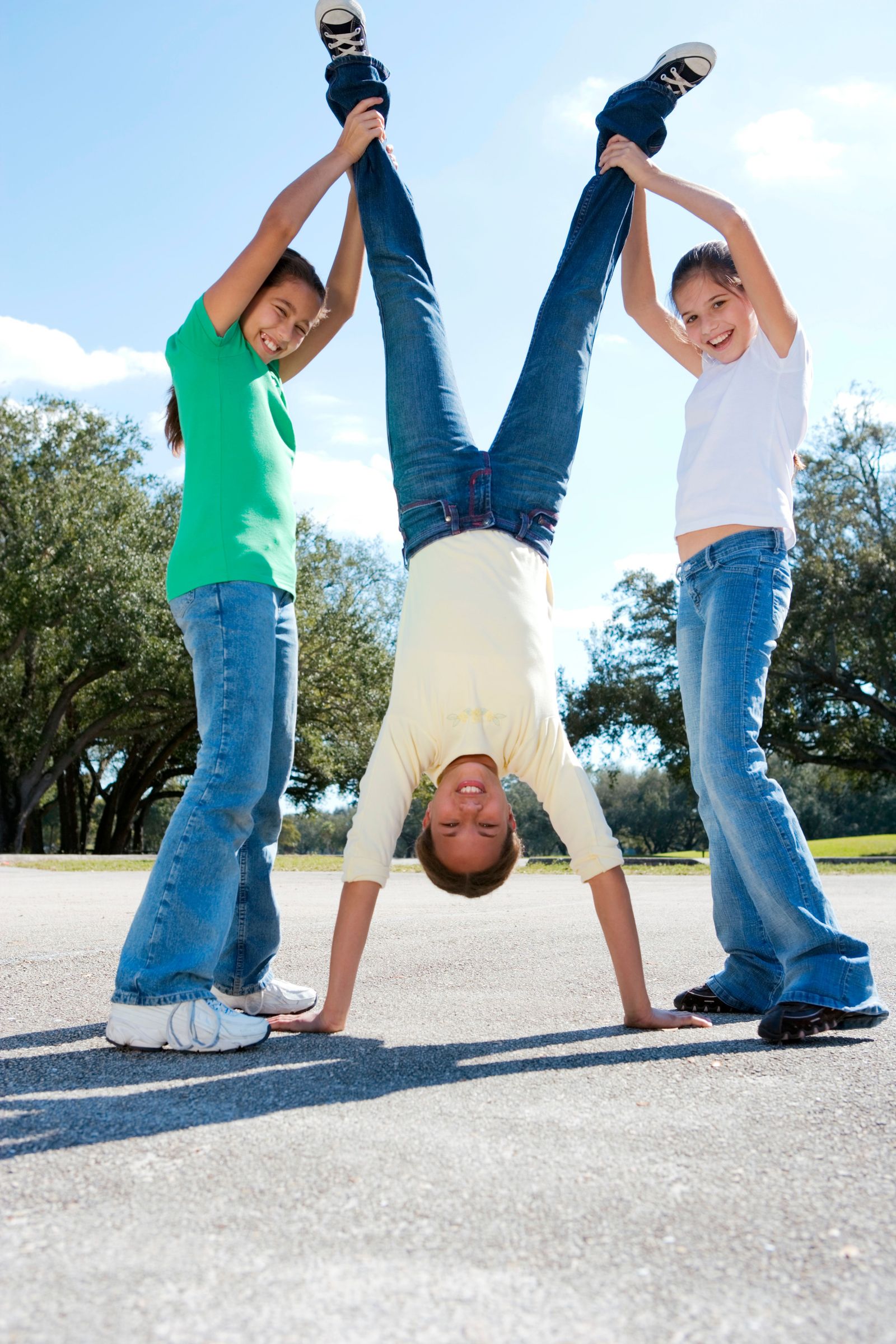 A child doing a handstand while two friends hold her legs up, laughing
