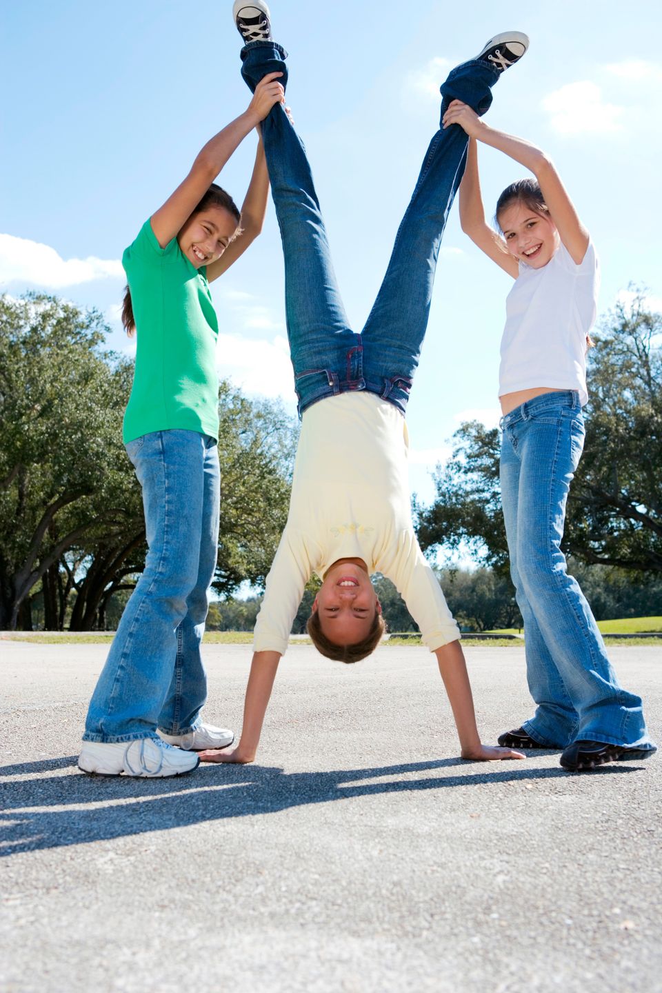 A child doing a handstand while two friends hold her legs up, laughing