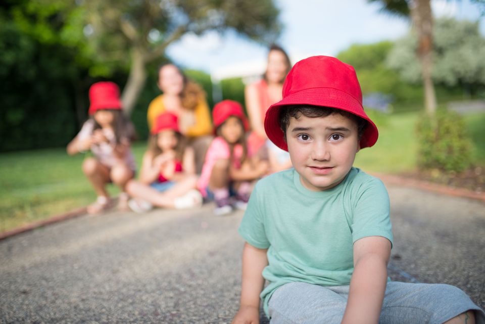 A young boy in a red bucket hat, with friends sitting behind him