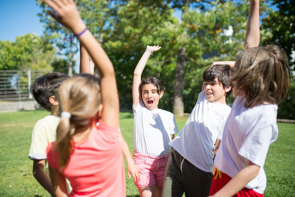 A group of children outdoors, arms raised and cheering together